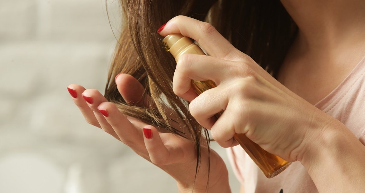 Mulher de cabelo castanho escuro aplicando óleo capilar na ponta do cabelo